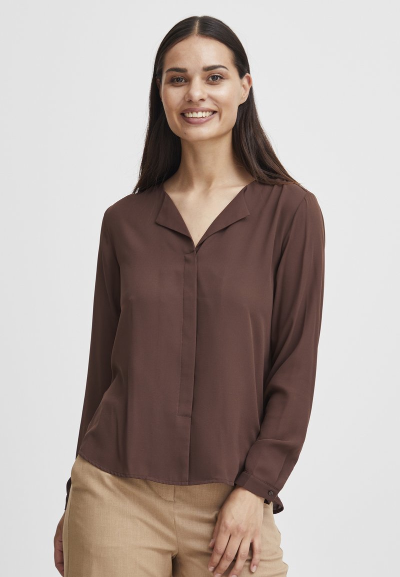 Blusa di seta marrone con scollatura a V profonda e maniche lunghe. Presenta una patta frontale e polsini con bottoni, abbinata a pantaloni beige.