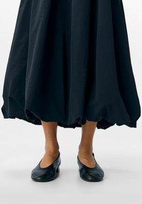 Falda negra, volumétrica, con dobladillo fruncido, combinada con zapatos planos de cuero negro. Tela texturizada y diseño de zapato liso.
