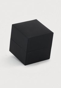 Kis fekete négyzet alakú ékszerdoboz levehető fedele van, fehér felületen elhelyezve.