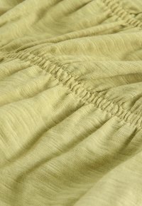 Gros plan d’un tissu vert clair avec des coutures élastiques froncées créant des lignes horizontales texturées et plissées.