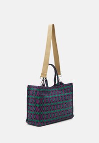 Torebka typu tote w wielokolorowym wzorze geometrycznym w odcieniach fioletu i zieleni, wykonana z materiału, z długim beżowym paskiem i czarnymi akcentami metalowymi.