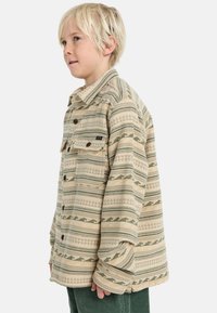 Camicia beige a fantasia con righe verdi e marroni, dotata di colletto, chiusura con bottoni e due tasche frontali con pattine.