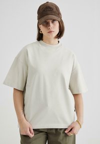 Light beige oversized cotton t-shirt with short sleeves, a round neckline, and side slits, paired with an embroidered brown corduroy cap.