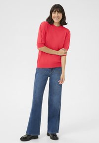 Haut corail à manches courtes avec un col montant, assorti à un jean bleu à jambes larges. La tenue présente une texture lisse et une coupe décontractée.