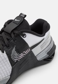 Černo-bílé sportovní boty Nike s tabulí "LOCK LACES", vlnitým designem na boku a textem o inženýrství pro šampionské sportovce.