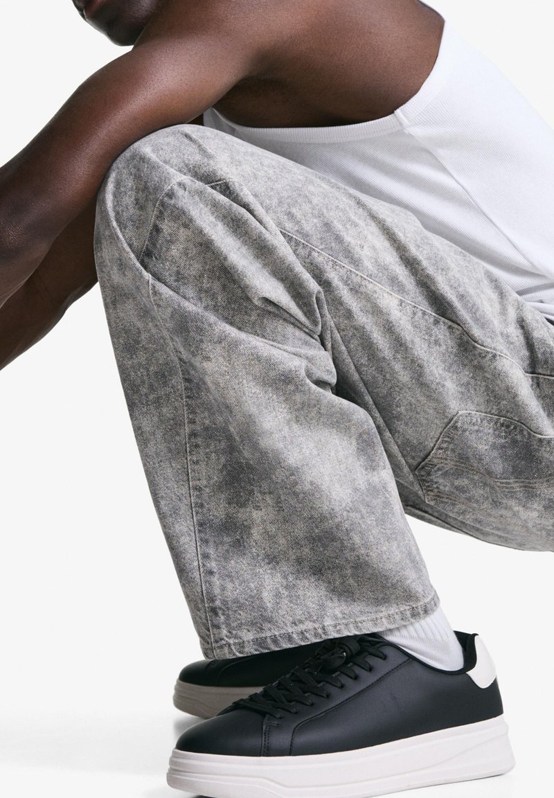 Graue Denim-Hosen mit strukturierter Optik, kombiniert mit schwarzen Ledersneakern mit weißen Akzenten und einer dicken Sohle.