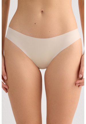 Kobieta ubrana w bezszwową, cielistą bieliznę w stylu bikini, pokazana od połowy tułowia do połowy uda, stojąca z rękami swobodnie opuszczonymi wzdłuż ciała.