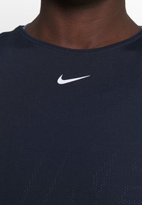 Mörkblå sporttröja i mjukt tyg med en vit Nike-logga på bröstet och diskret prickmönster.