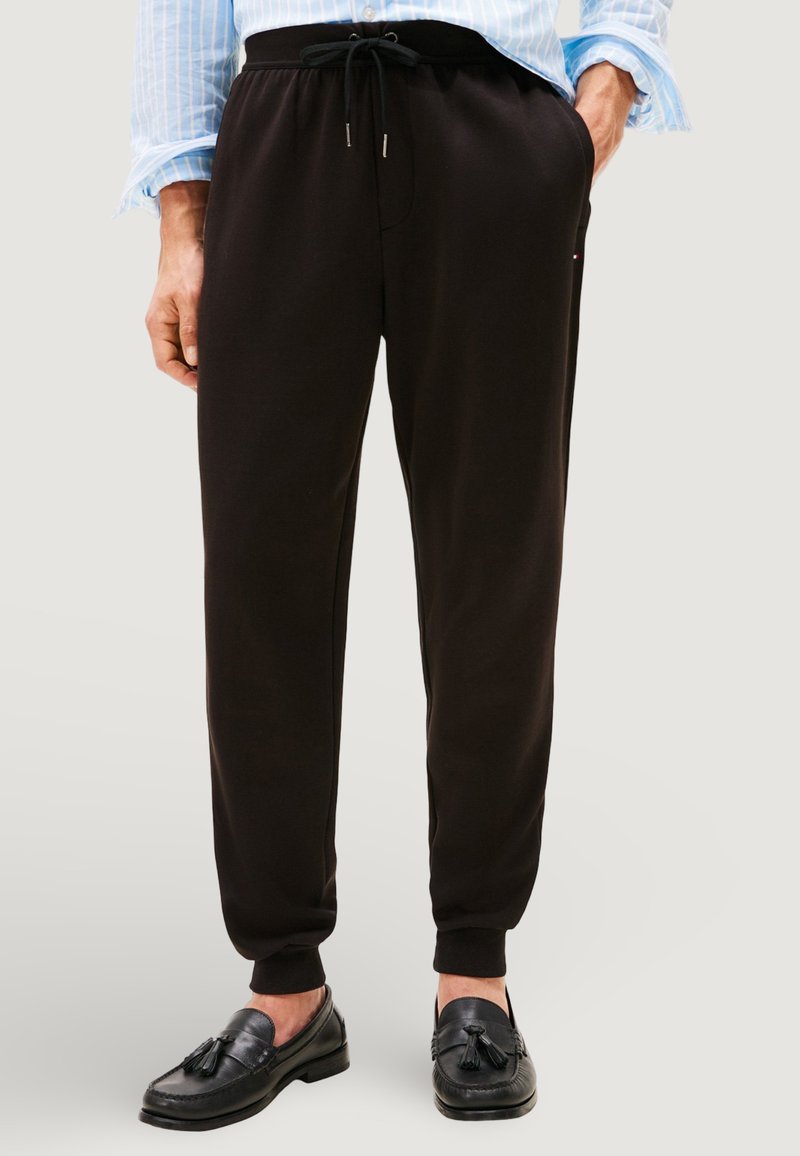 Pantaloni della tuta neri realizzati in tessuto morbido, con vita elasticizzata e coulisse, gambe affusolate e polsini alla caviglia a costine.