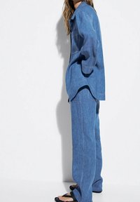 Vaateyhdistelmä vaaleansinisestä denimistä, jossa on löysä paita ja leveälahkeiset housut näkyvillä ompeluseikoilla. Sandalit viimeistelevät ilmeen.