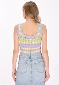 Top de punto lila sin mangas con bordes en forma de concha, que presenta rayas horizontales en verde y amarillo. Combinado con una falda de mezclilla azul claro.