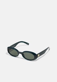 Oval sunglasses in dark green plastic, featuring tinted lenses and a gold rectangular accent on the frame. Smooth texture and sleek design.