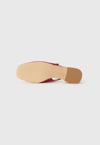 Røde skinnhøye hæler med en glatt overflate, spiss tå og en solid beige såle som har et teksturert grep.