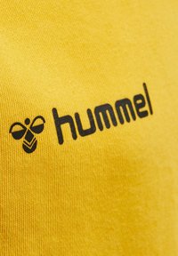 Gul bomulls tyg med en svart tryckt logotyp som har ett bi-motiv och ordet "hummel" tydligt synligt.