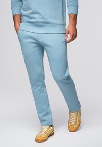 Lichtblauwe sweatpants gemaakt van zachte stof hebben een taps toelopend ontwerp, een elastische tailleband en minimalistische zijzakken, gecombineerd met gele sneakers.