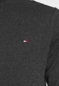 Maglione grigio lavorato a maglia con texture a coste, caratterizzato da un piccolo logo ricamato in rosso, bianco e blu nella zona sinistra del petto.