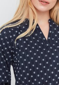 Top blu navy realizzato in tessuto leggero, caratterizzato da un motivo a strisce verticali e piccoli motivi bianchi. Collo a V e texture morbida.