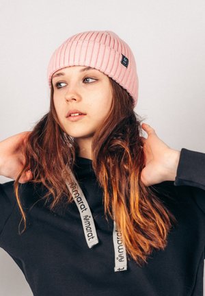 Pink ribbed knit beanie with a folded cuff, worn with a black hooded sweatshirt featuring gray drawstrings. Simple, functional, and cozy design.