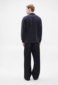 Μπλε ναυτικό φούτερ με ριμπ γιακά και μανσέτες, συνδυασμένο με φαρδιά σκουρόχρωμα τζιν από denim με πίσω τσέπες και λεία υφή.