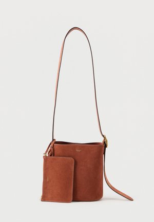 Bolso tipo saco de ante marrón de Coach con correa ajustable y bolso con cremallera a juego sobre fondo blanco.