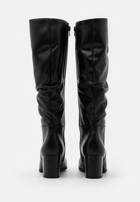 Black knee-high boots made of smooth leather with a fitted design, slouchy texture, rear zipper closure, and chunky heels.