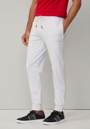 Lichtgrijze sweatpants met een elastische tailleband en trekkoord, voorzien van zijzakken en een klein rood logo. Gepaard met zwartgrijze sneakers.