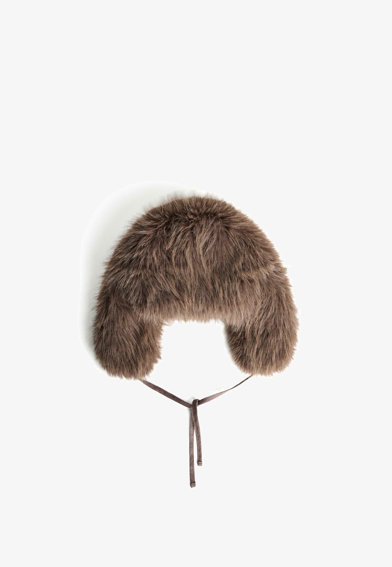 Cappello in finta pelliccia marrone con paraorecchie; texture morbida, forma arrotondata e un legaccio centrale per una vestibilità sicura. Dettagli in pelliccia lunga molto evidenti.