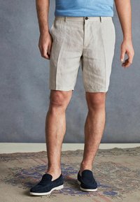 Pantaloni scurți din in, de culoare bej deschis, cu o croială lejeră, având buzunare frontale și închidere cu un singur nasture. Asortați cu pantofi slip-on bleumarin.