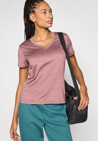 Μπλουζάκι με V σε απαλό ρόζ χρώμα, κατασκευασμένο από απαλό, υφασμάτινο ύφασμα με υφή. Συνδυάζεται με παντελόνια τυρκουάζ, αξεσουάρ με μαύρη τσάντα ώμου.