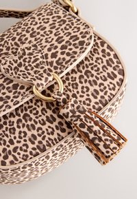 Leren handtas met een beige achtergrond en bruine luipaardprint. Heeft een hartvormig slot en een kwastdetail bevestigd aan de riem.