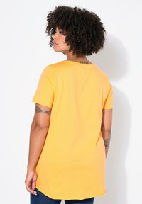 T-shirt jaune à manches courtes en tissu doux, avec un col rond et une coupe décontractée, dotée d'un ourlet arrondi et d'un design minimaliste.