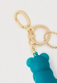 Μπρελόκ αρκούδας από σιλικόνη σε τιρκουάζ χρώμα με χρυσούς μεταλλικούς κρίκους και αλυσίδα, με κούμπωμα τύπου αστακού και διακοσμητικά χάντρες. Πλάτη της αρκούδας.