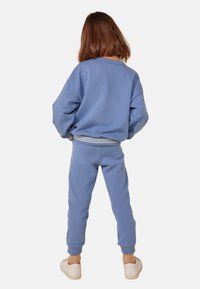 Modré mikina a odpovídající souprava tepláků vyrobená z měkké látky, s volným střihem a pruhovanými akcenty na pasu a manžetách.