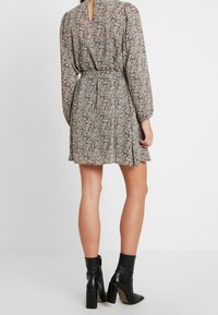 Vestido floral de manga corta con cintura ajustada, espalda con abertura y falda en capas. Hecho de un tejido ligero en tonos tierra. Botas negras de tacón.