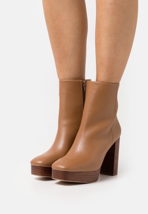 Hellbraune Leder-Stiefeletten mit abgerundeter Spitze und seitlichem Reißverschluss. Ausgestattet mit einem klobigen Holzabsatz und Plateausohle für zusätzliche Höhe.