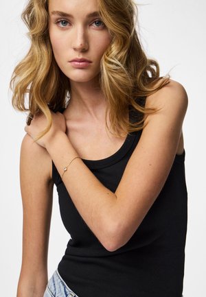 Svart ribbad linne, matchat med en ljusblå denimkjol. Ett delikat guldarmband med en liten berlock på handleden. Långt, vågigt blont hår.