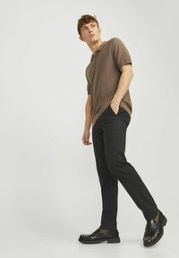 Polo shirt marrone a maniche corte con un motivo testurizzato, abbinato a pantaloni neri slim-fit e scarpe nere lucide. Design semplice e moderno.
