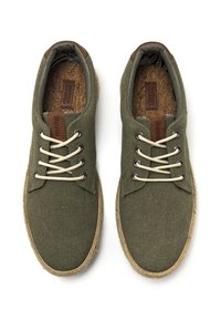 Zapatillas de lona verdes con cordones beiges, detalles de cuero marrón, plantillas de corcho texturizado y suelas envueltas en yute. Diseño de punta redonda.