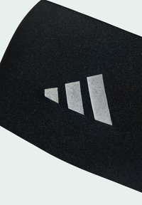 Černá tkanina s hladkým povrchem s metalickým stříbrným logem ve tvaru tří pruhů. Pruhy se liší šířkou a úhlem.