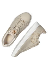 Baskets en cuir beige avec des accents dorés, présentant un motif texturé et une semelle en caoutchouc blanc, un design à lacets et un détail de marque sur le côté.