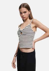 Stribet strik cropped tanktop i sort og hvid med twist-front detalje og spaghetti-stropper. Sammen med sorte træksnorsbukser.
