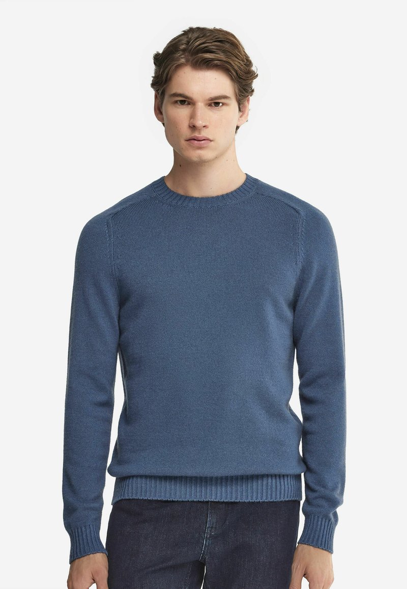 Blå stickad tröja med rund halsringning, ribbade ärmslut och fåll. Tyget verkar mjukt med en slät textur, figursydd design.