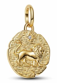 Zlati obesek z dvignjenim dizajnom leva in majhno zvezdasto diamante nad njim na teksturirani okrogli podlagi.