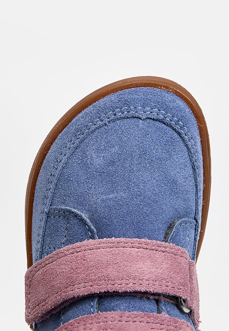 Nahaufnahme eines blauen Wildlederschuhs für Kinder mit brauner Sohle und einem rosa Wildleder-Klettverschlussriemen oben.
