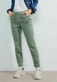 Pantalones jogger verde claro con cintura elástica, cordón, bolsillos laterales y piernas ajustadas, combinados con zapatillas color crema.