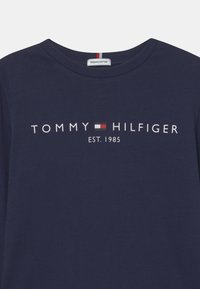 Námorně modré tričko z organické bavlny s kulatým výstřihem, s bílým textem "TOMMY HILFIGER" a "EST. 1985", s centrálním červeným a bílým vodorovným pruhem.