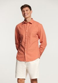 Camisa de rayas rojas y blancas de manga larga con botones en el frente, cuello y tejido texturizado, combinada con pantalones cortos blancos.