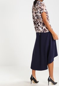 Blusa a maniche corte con stampa floreale in morbido tessuto leggero, abbinata a una gonna blu navy lunga fino al ginocchio, completata da tacchi alti neri.