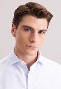 Camicia azzurro chiaro con colletto, vista ravvicinata che mette in evidenza la texture liscia e i piccoli bottoni bianchi sulla patta.