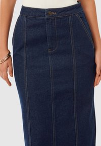 Fustă din denim închis, cu talie înaltă, buzunare frontale și cusături contrastante pe margini. Închidere cu nasture la talie.